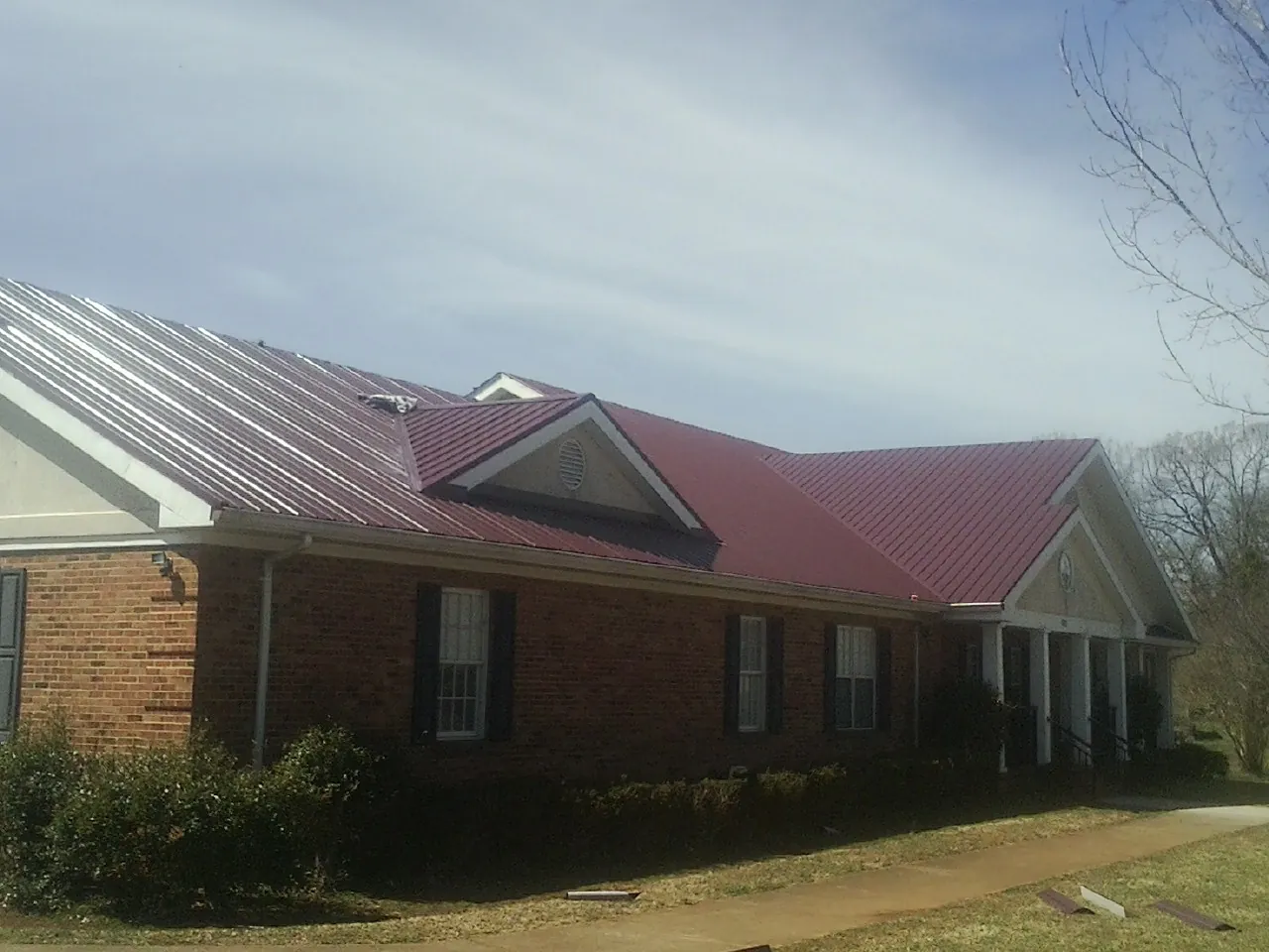 Red metal roof with gabled entries on a long brick building, from a Hail Damage Roof Repair job in Tarentum
