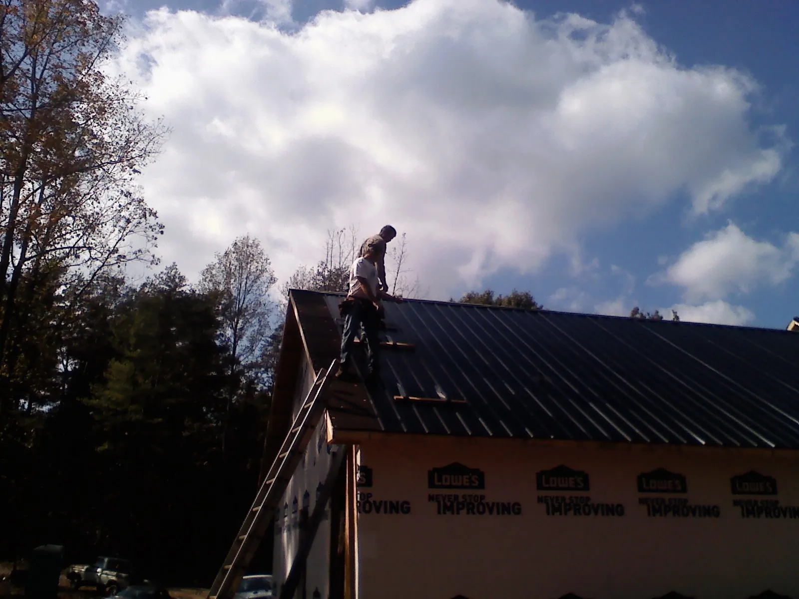 Roofer fastening dark metal panels high against a cloudy sky, from a Roof Inspection job in Tarentum