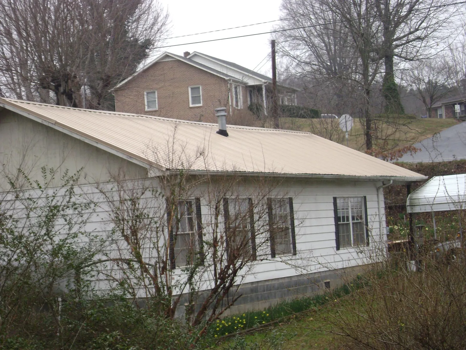 Tan metal roof on a white sided house set into a hillside — Commercial Roofing by Roofing Brothers in Tarentum